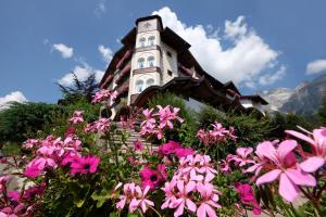 una casa con una torre dell'orologio e fiori rosa di Hotel Letizia a San Martino di Castrozza