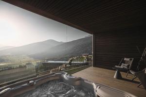 a bathroom with a tub with a view of a mountain at Alpin Panorama Hotel Hubertus in Valdaora
