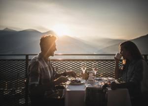 a man and woman sitting at a table with wine glasses at Alpin Panorama Hotel Hubertus in Valdaora