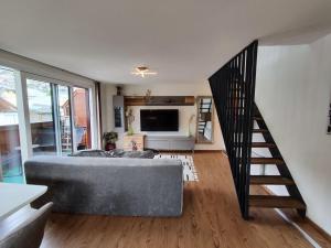 a living room with a grey couch and a staircase at Alpinoase City Centre Zell am See in Zell am See