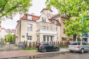 Deux voitures garées devant une grande maison dans l'établissement DR Apartments - Salt, à Sopot