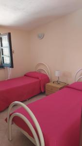 a bedroom with two beds with red sheets and a table at La Rosa dei Venti B&B in Chia