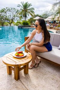 una mujer sentada en un sofá junto a una mesa con un plato de fruta en Luxury Vacation Rentals At Hacienda Pinilla en Tamarindo