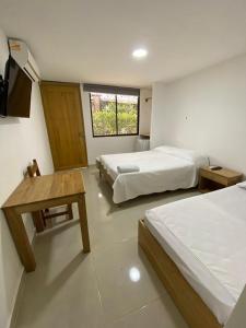 a bedroom with two beds and a table and a window at ApartaHotel Los Naranjos in Apartadó