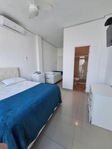 a white bedroom with a blue bed and a bathroom at Suítes Pitangueiras in Guarujá
