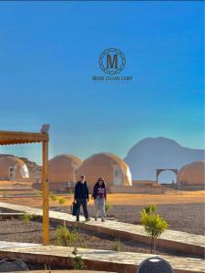duas pessoas a andar por uma estrada em frente a cúpulas em Moon Island Camp em Wadi Rum