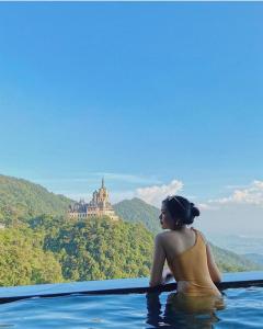 a woman sitting in a infinity pool looking at a castle at Venus Hotel Tam Đảo in Tam Ðảo