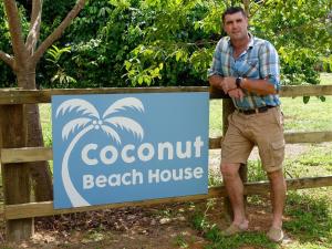ケープ・トリビュレーションにあるCoconut Beach Houseの浜辺の看板の横に立つ男
