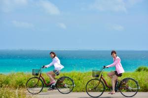 Dos mujeres montando en bicicleta en un camino cerca del océano en Haimurubushi, en Kohama