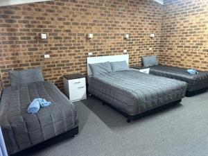 two beds in a room with a brick wall at Clock Tower Motor Inn in Coonabarabran