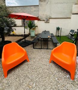 Duas cadeiras cor-de-laranja, uma mesa e um guarda-chuva. em ESCAPADE en CHAMPAGNE em Épernay