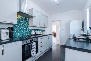 a kitchen with white cabinets and black counter tops at "Eastville Court Rhyl" by Greenstay Serviced Accommodation - Cosy 2 Bedroom Bungalow with Parking, Netflix & Wi-Fi, Close To Beaches, Shops & Restaurants - Ideal for Families, Business Travellers & Contractors in Rhyl