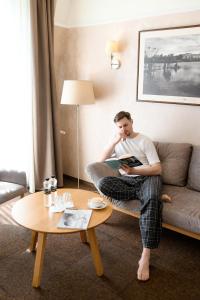 Ein Mann, der auf einer Couch sitzt und ein Buch liest. in der Unterkunft Nota Bene Hotel & Restaurant in Lwiw