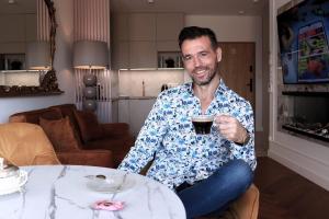 un homme assis à une table tenant une tasse de café dans l'établissement Pratum Pink&Blue Mikołajki Apartament de lux z kominkiem, prywatnym pomostem i 400m strefą wellness, à Mikołajki