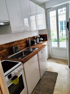 a kitchen with white cabinets and a sink and a window at Charmant logement à Luc-sur-Mer - 100m de la Plage in Luc-sur-Mer