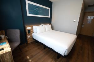 Un pequeño dormitorio con una cama blanca y una silla en Travelodge Madrid Metropolitano, en Madrid