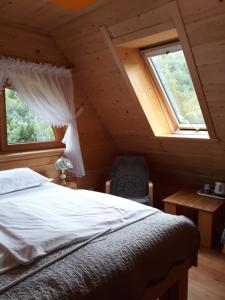 a bedroom with a bed and a chair and two windows at Drewniana Oaza in Ochotnica Dolna