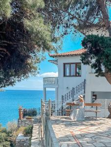 a woman sitting in front of a house next to the ocean at ClubOrsa Ourania's Mansion in Skiathos Town