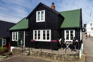 ein schwarzes Haus mit grünem Dach und zwei Menschen sitzen vorne in der Unterkunft A pearl in the center of the center of Thorhavn in Tórshavn