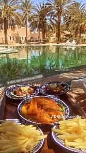 a table with plates of food next to a swimming pool at Hotel Pansy in Ksar Ghilane