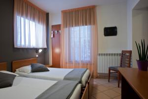 a hotel room with two beds and a desk at Hotel Oasi Verde in Bienno
