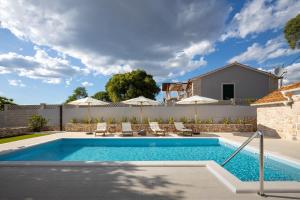 a swimming pool in a yard with chairs and umbrellas at Villa Casa di Perla in Primošten