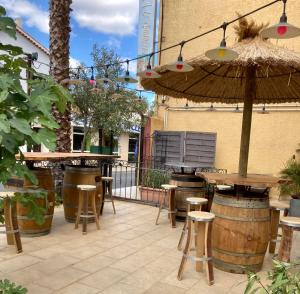 an outdoor patio with tables and stools and an umbrella at Hôtel Le Gambetta in Vias