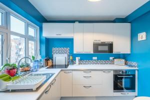 a kitchen with blue walls and white cabinets at Comfortable Home in Wandsworth by UndertheDoormat in London