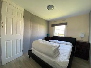 um quarto com uma cama com lençóis brancos e uma porta em Homely Caravan Just A Short Walk To Hembsy Beach In Norfolk Ref 00036ba em Hemsby