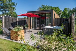 a small house with a red umbrella and a patio at Wellnesslodge Merel in Dalerveen