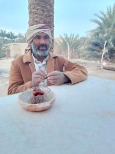 Tanirt ecolodge في سيوة: رجل يجلس على طاولة مع وعاء من الطعام