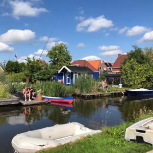 two people sitting on a dock with boats in the water at Vakantie Studio Grou in Grou