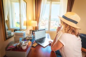 una mujer con sombrero sentada en un escritorio con un portátil en BRISTOL Hotel Opatija, en Opatija