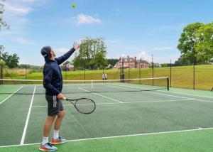 un hombre sirviendo una pelota de tenis en una pista de tenis en The Astbury Golf And Lodge Resort, en Bridgnorth