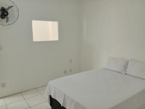 Cama blanca en habitación blanca con ventilador en Angelus Hotel & Estacionamento, en Campos dos Goytacazes