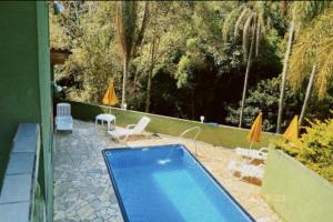 einen Pool im Garten mit Stühlen und Sonnenschirmen in der Unterkunft Chácara Paraíso in Mairiporã