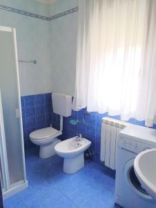 Baño de azulejos azules con aseo y lavamanos en Fides Apartment, en Rosolina Mare