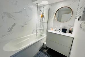 a white bathroom with a tub and a sink and a mirror at Cosy flat 2 steps from the port 4pers in Gujan-Mestras