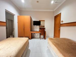 a bedroom with two beds and a desk with a television at Hotel Caravan Tanah Abang in Jakarta