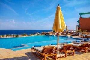 a pool with chairs and an umbrella and the ocean at Outstanding Red Sea View-Brand New Azzurra Apartments in Hurghada