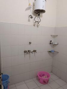 baño de azulejos blancos con cubo y ventilador en Mahadev Kripa sadan Homestay & Guest house, en Ayodhya