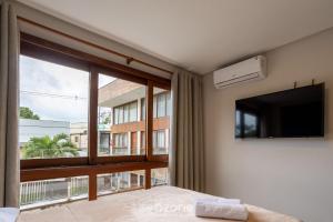 um quarto com uma grande janela e uma televisão de ecrã plano em CPR - Apartamentos a 200m da praia com Piscina em Maraú