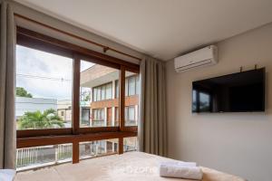 a bedroom with a large window and a flat screen tv at CPR - Apartamentos a 200m da praia com Piscina in Marau