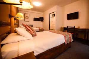 ein Hotelzimmer mit einem Bett mit weißer Bettwäsche und Kissen in der Unterkunft Hotel Raymi in Cusco