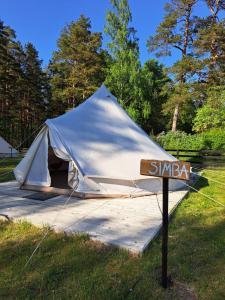 biały namiot z znakiem w trawie w obiekcie Glempings Bērzciema Lagūna w mieście Bērzciems
