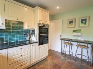 una cocina con armarios blancos y 2 taburetes en Striding Home, en Ambleside