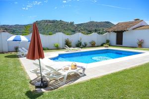 a swimming pool with an umbrella and two lawn chairs and an umbrella at Amplia casa rural con precioso jardín cerca de Málaga capital. in Málaga