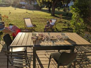 a picnic table with wine glasses and a woman sitting in a chair at Maison/appartement proche Cala Rossa in Lecci