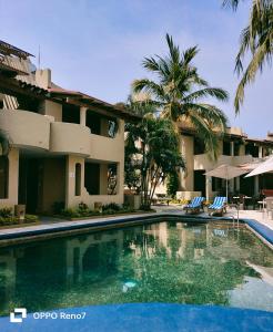 a swimming pool in front of a building with palm trees at Villas Miramar in Zihuatanejo