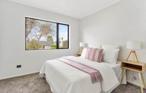 a white bedroom with a bed and a window at Holiday Home at Huia Road in Auckland